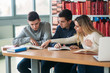 © Aleksandr - University students sitting together at table with books and laptop. Happy young people doing group study in library