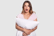 © sementsova321 - Astonished woman gets up at night, has shocked expression after seeing nightmare, holds pillow, tries to protect herself, isolated over white background. Omg, its awful! People and surprisement