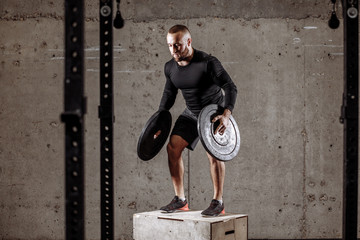 a sporty male is holding two weight plates and looking down