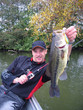 © sablin - Scène de pêche en eau douce. Pêcheur au leurre en casting tenant un gros black bass. pêche en bateau