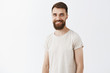 © Cookie Studio - Happy creative and young bearded male coworker with stylish hairstyle in white casual t-shirt smiling joyfully standing over gray background talking about new company concepts creating new ideas