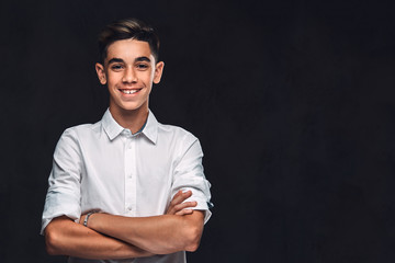 Handsome young guy dressed in white shirt standing with crossed arms. Isolated on the dark background.