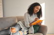 © Anatoliy Karlyuk - Indoor shot of trendy looking young African American woman wearing ripped jeans lying on comfortable sofa in living room and writing down in diary, making grocery list before going shopping