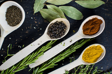 White spoons with spices are on a black wooden table