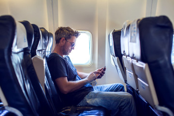 Man is reading text message on mobile phone and speaking by phone during flying in the airplane