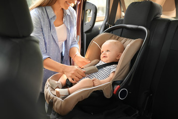 Mother fastening baby to child safety seat inside of car