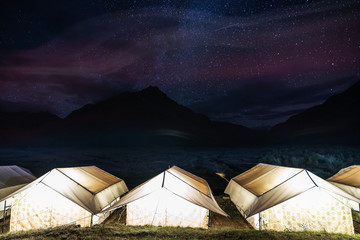 Wall Mural - camping under colourful sky full of stars. glowing tents with silhouette mountains and sky full of s
