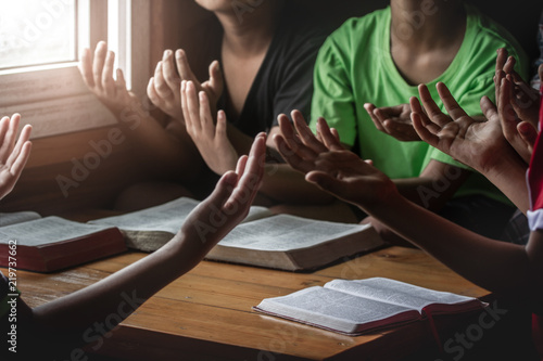 Fotografie, Obraz christian children group praying together around wooden table with bible in home