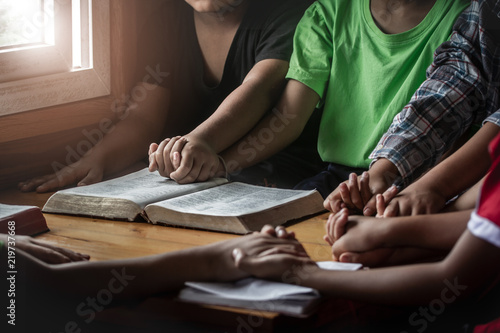 Fotografía children group praying together around wooden table with open bible page in home