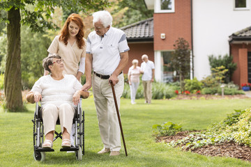 Wall Mural - An elderly disabled couple with their caretaker in the garden outside of a private rehabilitation clinic.