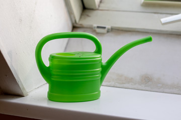 Green small watering can on a windowsill inside 