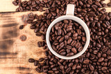 Fototapeta Mapy - Cup of coffee full of coffee beans on wood background, top view