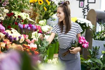 Wall Mural - Cheerful young florist at work. Woman picking flowers for bouquet