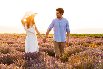 Photo of romantic young man and woman, walking together outdoor in lavender field