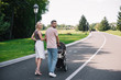 © LIGHTFIELD STUDIOS - back view of parents walking with baby carriage on road in park and looking at camera