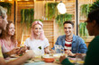 © pressmaster - Four companions looking at their friend during conversation by festive dinner in cozy cafe