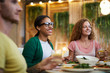 © pressmaster - Two happy intercultural girls sitting by served festive table at dinner and talking