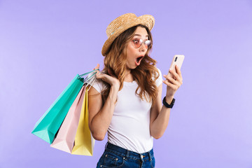 Canvas Print - Screaming cute woman isolated over purple wall background holding shopping bags using mobile phone.