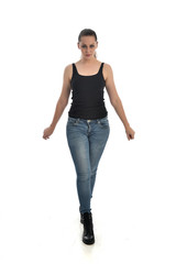 full length portrait of brunette girl wearing black single and jeans. standing pose facing the camera. isolated on white studio background.