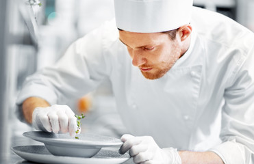 Wall Mural - food cooking, profession and people concept - happy male chef cook serving plate of soup at restaurant kitchen