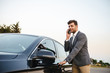 © Drobot Dean - Smiling young businessman in suit standing at his car