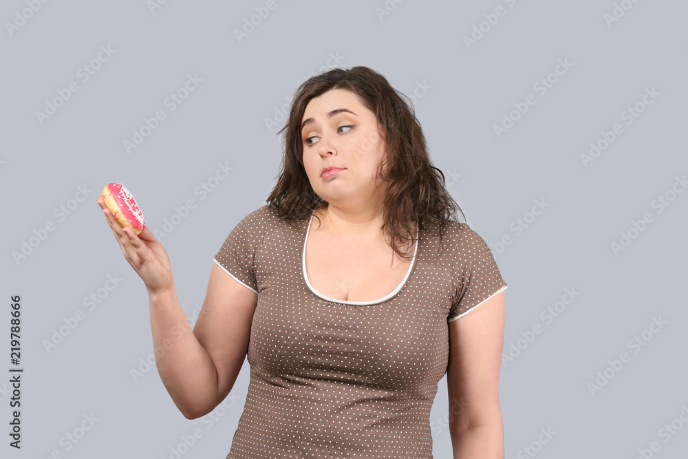 Young stout woman with donut on grey background. Diet food concept