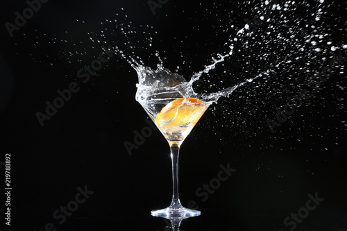 Fotografía Glass with splashing cocktail and slice of orange on black background