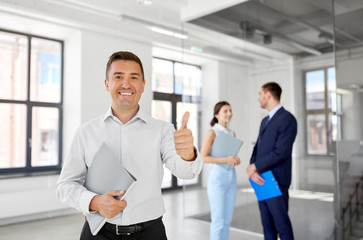 Poster - real estate business, sale and people concept - happy smiling realtor or businessman with folder showing thumbs up and customers at new office room