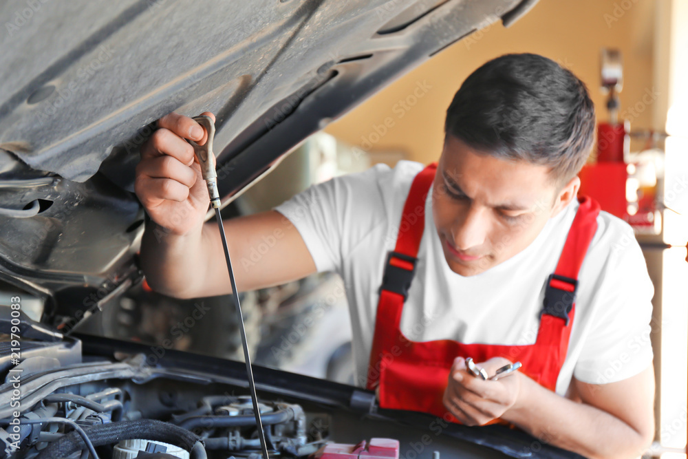 Male mechanic checking level of oil in car engine
