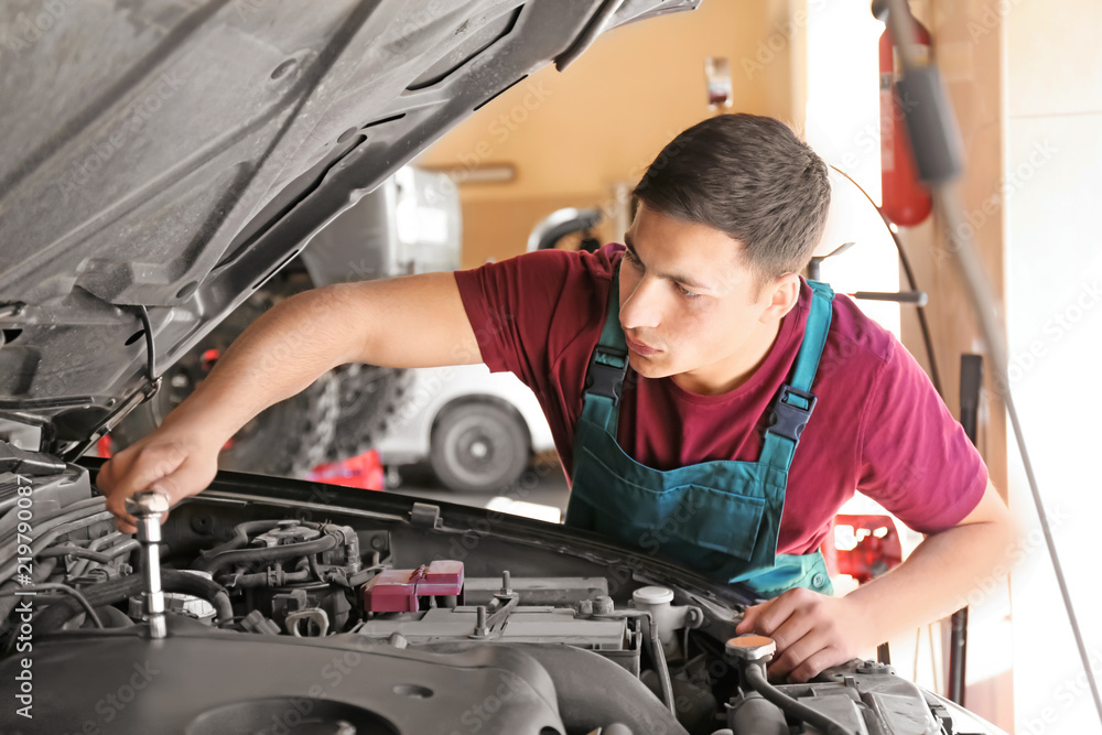 Young auto mechanic repairing car in service center