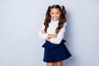 Back to school! Nice cute tender cheerful adorable lovely stylish girl with curly pony-tails in white formal blouse and dark blue skirt, folded arms. Isolated over grey background
