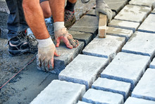 A Workman's Gloved Hands Use A Hammer To Place Stone Pavers. Worker Creating Pavement Using Cobblestone Blocks And Granite Stones.