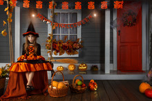 Funny Girl Child Kid In Halloween Witch Costume With Black Hat And Orange Pumpkins Basket With Spooky Face For Candies And Sweets Sitting On Swing Ready For Celebration Autumn Holiday Halloween.