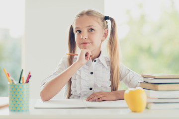 Close up photo portrait of little intelligent learner looking up touching chin solving text task exam sitting at table in light white modern indoor class room doing home work