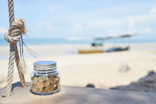Gold Coin In Bottle On Swing With Sea And Beach Background, Growth For The Save Money Concept