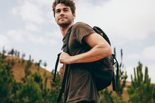 Man Walking Through A Forest Wearing A Backpack.