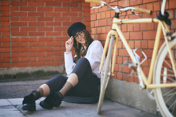 Wall Mural - Woman sitting on sidewalk and using smart phone. Next to her yellow bicycle.