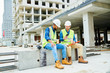 © Seventyfour - Full length portrait of two workers wearing hardhats  chatting and using smartphone during coffee break on construction site, copy space