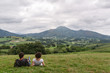 © Esther Pueyo - Pareja joven descansando en lo alto de una colina verde y mirando a un bonito paisaje montañoso. Pirineos, España.