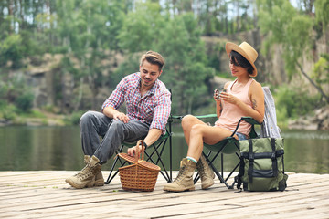 Canvas Print - Young couple resting on pier near lake. Camping season