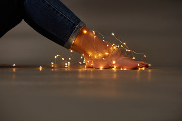 Beautiful female legs with bright garlands on the floor around a dark background with copy space