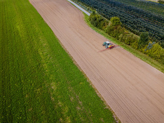 Wall Mural - Aerial view of tractor on farmland spraying fertilizer on a brown field.
