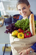 © lenets_tan - Young woman holding grocery shopping bag with vegetables .Standing in the kitchen