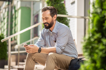 Wall Mural - Smiling bearded man using his smartphone on the porch