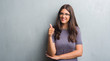 © Krakenimages.com - Young brunette woman over grunge grey wall wearing glasses happy with big smile doing ok sign, thumb up with fingers, excellent sign