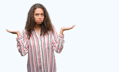 Wall Mural - Beautiful young hispanic woman clueless and confused expression with arms and hands raised. Doubt concept.