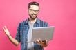 © denis_vermenko - Confident business expert. Confident young handsome man in shirt holding laptop and smiling while standing against pink background