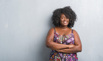 Young african american woman over grey grunge wall wearing colorful dress happy face smiling with crossed arms looking at the camera. Positive person.