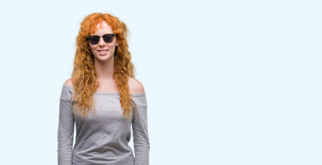 Sticker - Young redhead woman wearing sunglasses with a happy face standing and smiling with a confident smile showing teeth