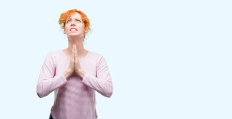 Sticker - Young redhead woman begging and praying with hands together with hope expression on face very emotional and worried. Asking for forgiveness. Religion concept.